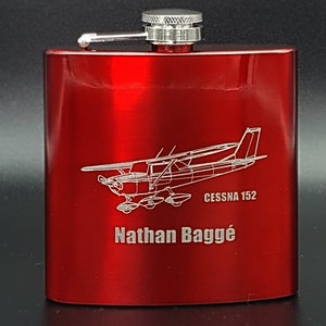 May include: Red metal hip flask with a silver lid and a silver engraved design of a Cessna 152 aircraft with the text "Cessna 152" and "Nathan Baggé".