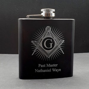 Könnte beinhalten: Schwarze Edelstahl-Taschenflasche mit silbernem Deckel und einem silbernen, gravierten Freimaurer-Symbol mit dem Buchstaben G in der Mitte. Der Text "Past Master Nathaniel Waye" ist unterhalb des Symbols graviert.