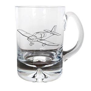 May include: A clear glass mug with a handle, featuring a line drawing of a small airplane. The mug has a rounded base.
