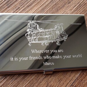 May include: A polished silver business card holder featuring an etched helicopter design. The inscription reads: "Wherever you are it is your friends who make your world Marco."