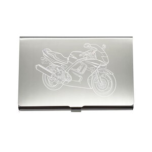 Könnte beinhalten: Ein silberner Visitenkartenhalter mit einer detaillierten weißen Strichzeichnung eines Sportmotorrads. Das Motorraddesign umfasst die Räder, den Auspuff und den Lenker. Der Kartenhalter hat eine schwarze Umrandung und einen Verschluss.