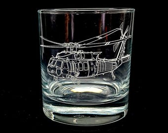 May include: A clear, lowball glass etched with a detailed outline of a helicopter. The white etching contrasts against the clear glass, showcasing the helicopter's rotors, body, and tail. The glass sits on a black surface.
