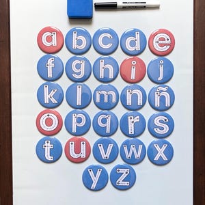 May include: A white magnetic whiteboard with a dark wood frame featuring a set of circular magnets, each displaying a lowercase letter of the alphabet with directional arrows for tracing. A blue rectangular eraser and a black dry-erase marker are included.