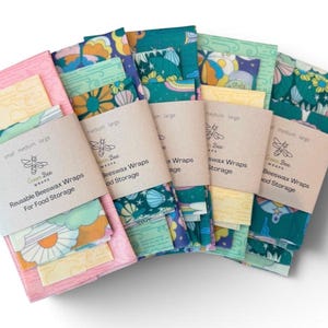 May include: Five sets of reusable beeswax food wraps, each secured with a beige paper band labeled Green Bee Wraps. The wraps feature colorful patterns including flowers, clouds, and shells in shades of pink, teal, yellow, and blue.