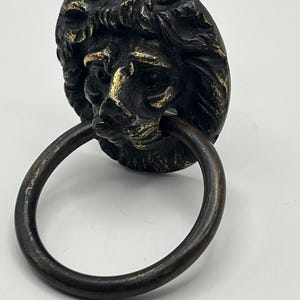 May include: A black and gold lion head door knocker with a ring pull. The lion's face is detailed and has a textured finish.