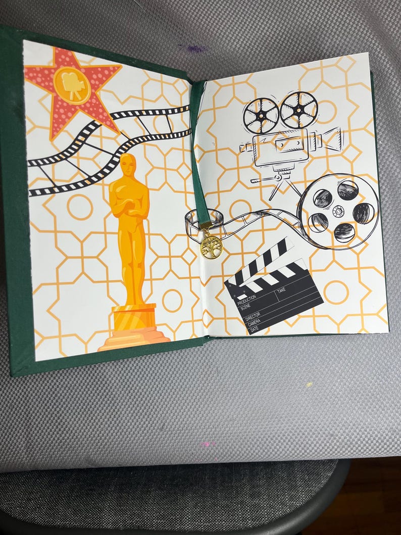K&ouml;nnte beinhalten: Offenes Buch mit gr&uuml;nem Einband. Die Seiten zeigen Illustrationen zum Thema Film, darunter eine goldene Oscar-Statue, ein roter Stern, Filmstreifen, eine Filmkamera und eine Filmklappe. Der Hintergrund hat ein geometrisches Muster.