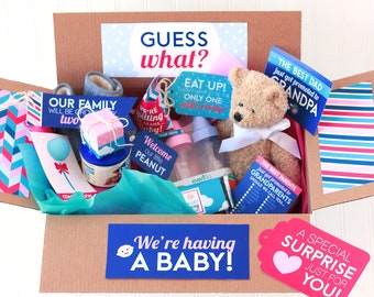 Può includere: Una scatola di cartone marrone con un annuncio di nascita blu e rosa che dice "We're having a baby!" La scatola è piena di articoli a tema baby, tra cui un orsacchiotto, una bottiglia, una piccola scatola regalo e una coperta a righe blu e rosa. Ci sono anche diversi biglietti con messaggi come "The Best Dad" e "Welcome our little peanut".
