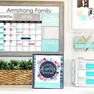 May include: A white calendar showing the month of April. The calendar is labelled "Armstrong Family". A binder with a floral design and the text "Our Family Binder" is on a shelf below the calendar. The binder is labelled "Armstrong Family".