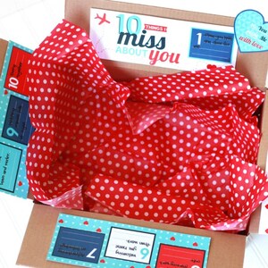 May include: A brown cardboard box with red and white polka dot tissue paper inside. The box has a blue and white label that says "10 things I miss about you". There are ten smaller labels with numbers 1 through 10, each with a different reason why the sender misses the recipient. The box also has a blue heart with the text "You Me with love".