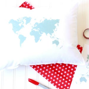 May include: A white pillow with a light blue world map printed on it. The pillow is lying on a red and white polka dot fabric.