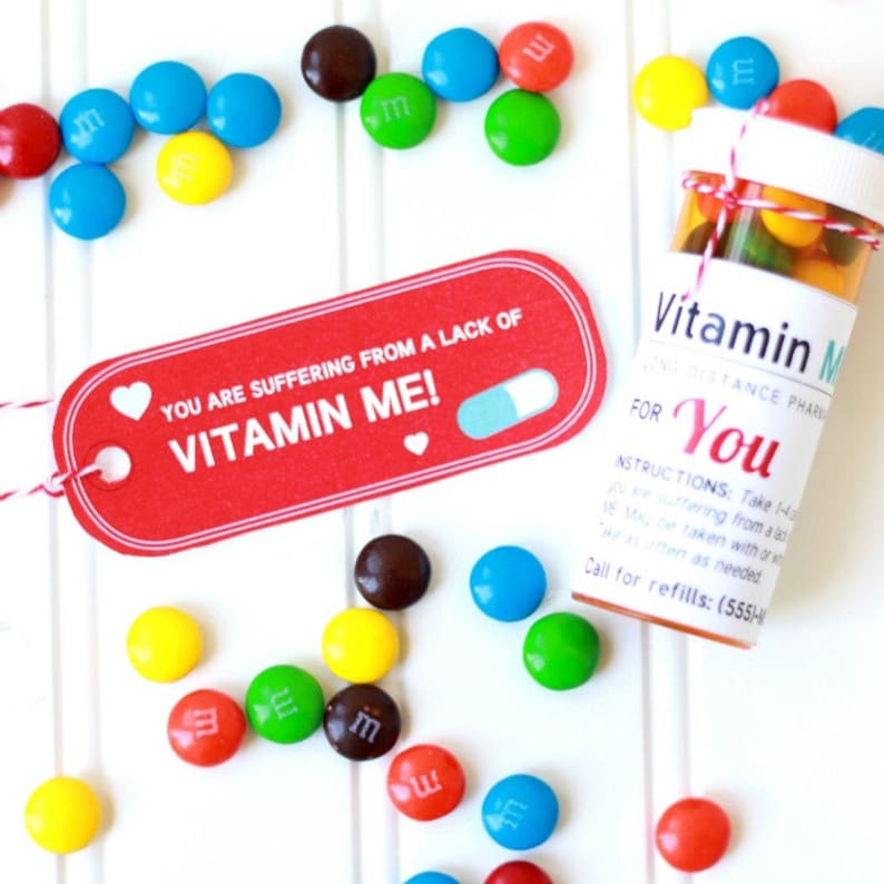 May include: A red and white pill-shaped tag with the text "YOU ARE SUFFERING FROM A LACK OF VITAMIN ME!"  A clear plastic bottle filled with colorful M&M's candies with a white label that reads "Vitamin Me" and "FOR You".