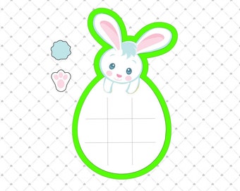 May include: A green cookie cutter shaped like a bunny rabbit peeking out of an egg. The bunny is white with blue eyes and pink ears. The egg is divided into sections by lines.