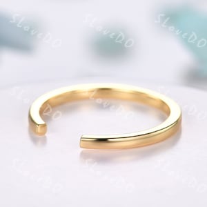 May include: A simple gold band ring with a slightly open end. The ring is smooth and polished.
