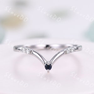 May include: A delicate silver ring with a V-shaped design. The ring features a small black gemstone at the point of the V and two smaller white gemstones on each side.