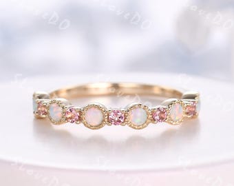 May include: A gold ring featuring alternating round opal and pink gemstone settings. The gemstones are set in a delicate band, creating a sparkling and elegant design. The ring is a piece of jewelry.