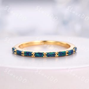 May include: A gold band ring with a row of blue and green opal stones set in a rectangular shape.