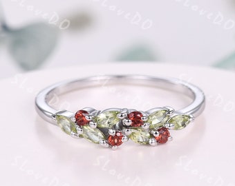 May include: A silver ring featuring a floral design with peridot and garnet gemstones. The ring has a delicate band and the gemstones are arranged in a leaf-like pattern. The ring is a piece of jewelry.