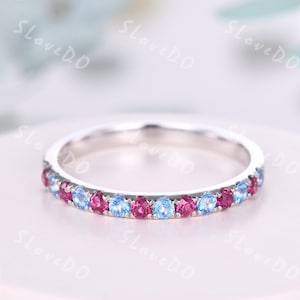 May include: A delicate silver band ring with a row of alternating blue and pink gemstones. The ring is set with small, round stones that create a subtle sparkle.