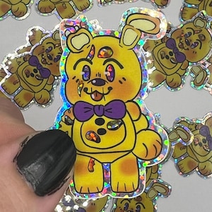 May include: A set of holographic stickers featuring a cartoon bear with a purple bow tie. The bear is yellow with brown spots and has a mischievous expression. The stickers are perfect for adding a touch of whimsy to laptops, water bottles, or journals.