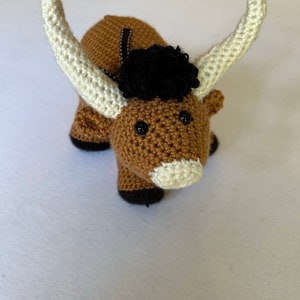 May include: A brown crocheted stuffed animal with white horns and black eyes. The animal has a black crocheted mane.
