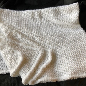 May include: A white crocheted blanket with a fluffy texture and a fringed edge.