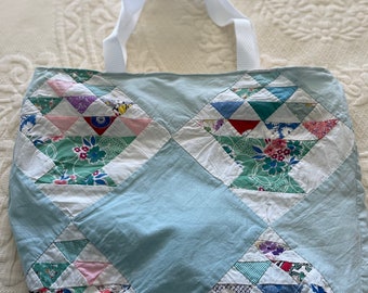 May include: A light blue tote bag made from patchwork fabric. The bag has a white handle and is decorated with a diamond pattern of colourful fabric triangles.