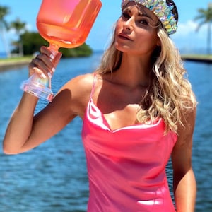 May include: A large, orange crystal singing bowl with a stem is held up. The bowl is a vibrant orange color and has a clear, iridescent stem. The person is wearing a pink satin dress and a jeweled crown.