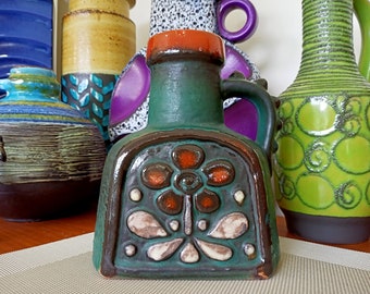 Könnte beinhalten: Eine grüne Keramikkanne mit braunem Henkel und einem Blumendesign in Braun-, Orange- und Weißtönen. Die Kanne hat eine strukturierte Oberfläche und eine glänzende Oberfläche.