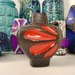 May include: A collection of vintage ceramic vases in various shapes and colors. The foreground features a dark brown vase with glossy red accents. Other vases in the background are teal, blue, purple, and white, showcasing diverse patterns and textures.