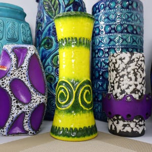 May include: A collection of colorful ceramic vases in various shapes and sizes. The vases feature vibrant colors like turquoise, yellow, purple, and black, with decorative patterns and textures. Some have a glossy finish, while others have a matte appearance.