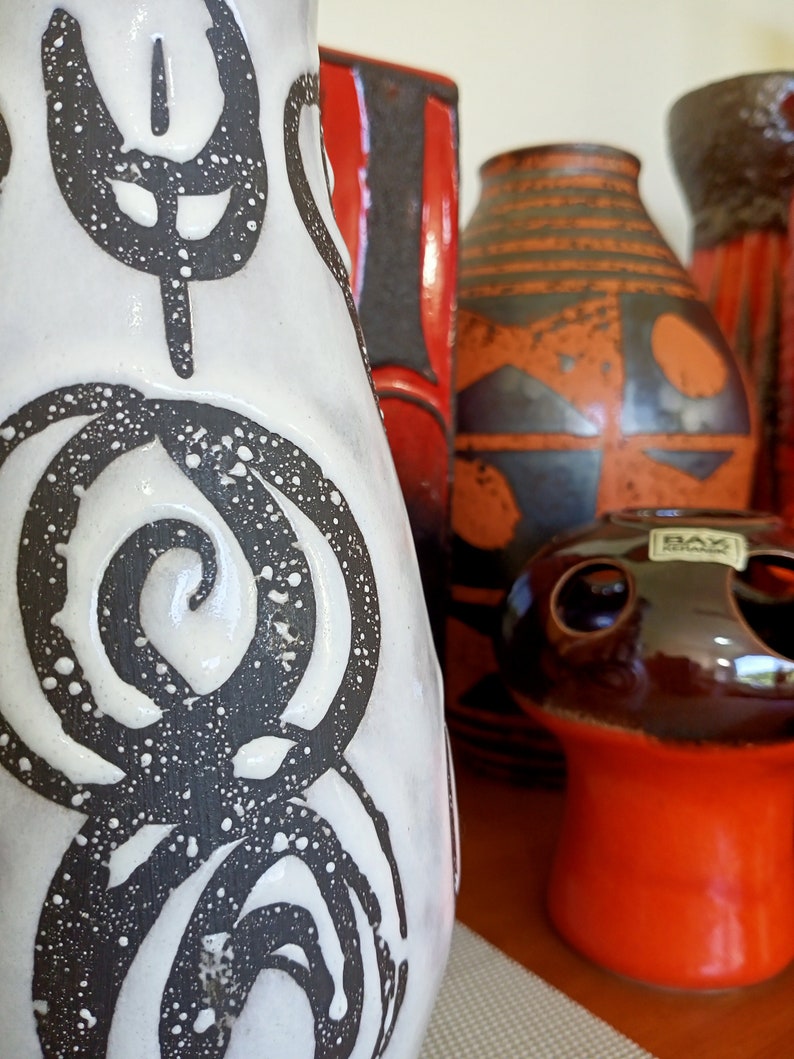 May include: A collection of ceramic vases in various shapes and sizes. The vases feature a range of colors, including white, black, red, and orange. Some vases have abstract patterns and designs, while others have a smooth finish. The collection includes a mushroom-shaped vase.