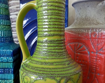 Könnte beinhalten: Eine grüne Keramikkanne mit strukturierter Oberfläche und einem Blumendesign. Die Kanne hat einen Henkel und eine breite Öffnung.