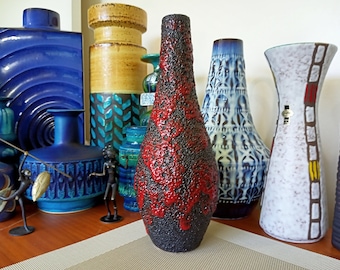 May include: A collection of vintage ceramic vases in various colors and patterns. The vases are arranged on a wooden table with a brown and white patterned placemat. The vases are all different shapes and sizes, and some have unique textures.