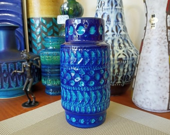 May include: A blue ceramic vase with a geometric pattern. The vase is decorated with a repeating pattern of triangles, circles, and dots. The vase is about 10 inches tall.