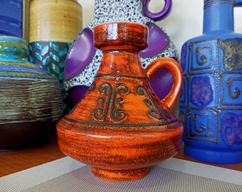 May include: A bright orange ceramic vase with a black design. The vase has a wide base and a narrow neck with a handle.
