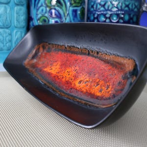 Peut inclure: Un bol en céramique noir de forme carrée avec un intérieur texturé et vibrant. L'intérieur présente un mélange de teintes orange, rouge et marron. Le bol est probablement vintage et fait partie d'une collection décorative.