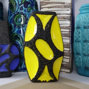 May include: A collection of ceramic vases featuring a central bright yellow vase with a black textured pattern, a purple and black vase, a blue patterned vase, a tall beige textured vase, a turquoise vase, and a partial orange and blue vase.