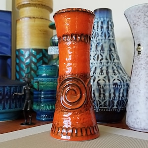 May include: A tall, orange ceramic vase with a swirl design. The vase has a glossy finish and is decorated with brown accents.