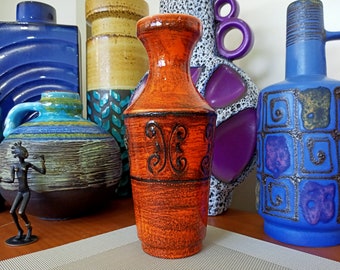 May include: Orange ceramic vase with a black floral design. The vase has a narrow neck and a wide base. It is surrounded by other colorful ceramic vases.