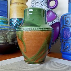 May include: A green and brown ceramic vase with a white rim and a decorative band of white dots. The vase has a rounded body and a narrow neck.