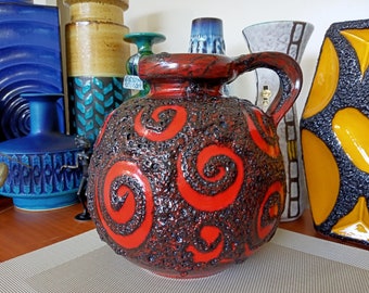 May include: A red and black ceramic vase with a textured surface and a swirling pattern. The vase has a handle and a wide opening.