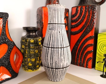 May include: A collection of vintage ceramic vases in various shapes and sizes. The vases feature bold colors like orange, black, and yellow, with textured and patterned designs. A tall white vase with black vertical stripes is in the center.