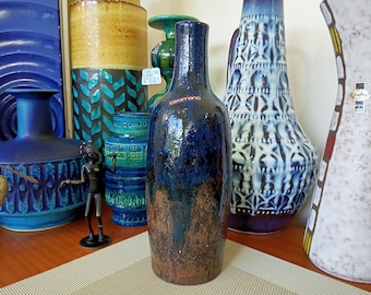 May include: A collection of blue and green ceramic vases with a brown and blue ceramic vase in the center. The vase in the center is labeled "ceramano".