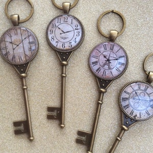 May include: Four antique-style keychains with clock faces. Each keychain features a different clock face design, including a Roman numeral clock, a clock with an Eiffel Tower design, and two clocks with intricate designs.