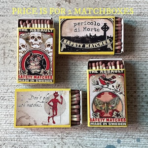 May include: Four vintage matchboxes with yellow borders. The matchboxes feature various designs, including skulls, a cat, a devil, and a butterfly. The text on the boxes includes "THE ASSAULT", "SAFETY MATCHES", and "MADE IN SWEDEN".