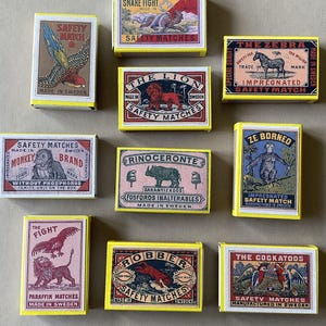 May include: A collection of vintage matchboxes with colorful illustrations and text. The boxes feature images of animals like a lion, zebra, monkey, and snake. The text includes phrases like "Safety Matches" and "Made in Sweden."