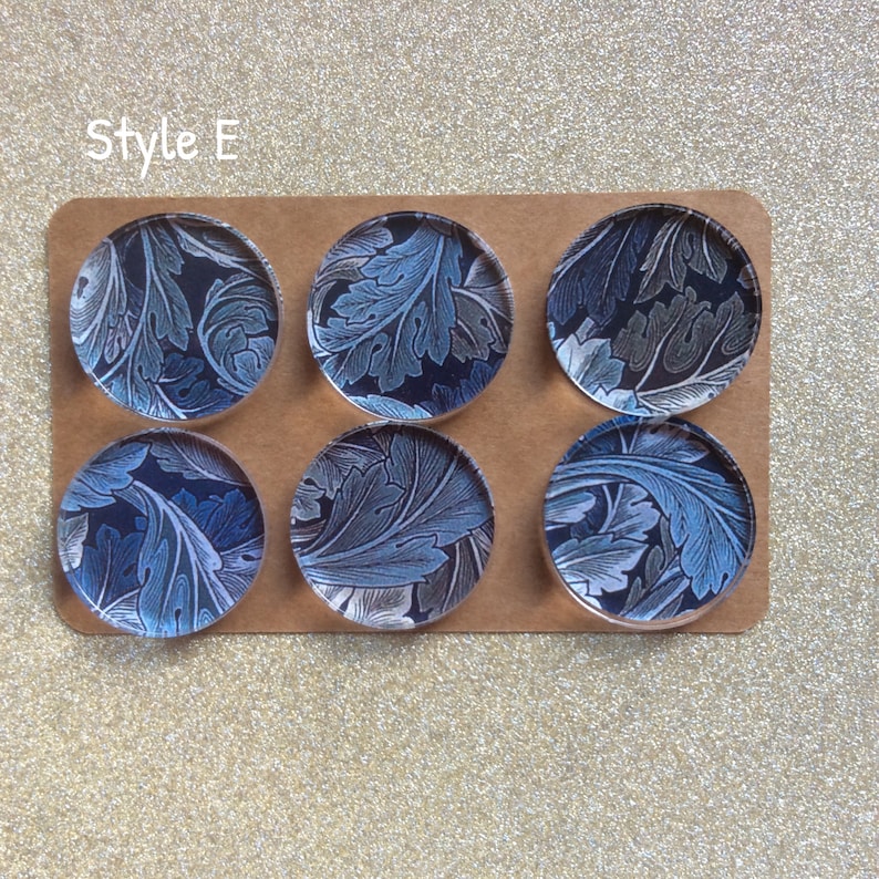 Puede incluir: Seis posavasos redondos de vidrio con un patr&oacute;n floral azul y blanco. Los posavasos est&aacute;n dispuestos en dos filas de tres sobre una superficie marr&oacute;n. El texto "Style E" est&aacute; impreso en la superficie.