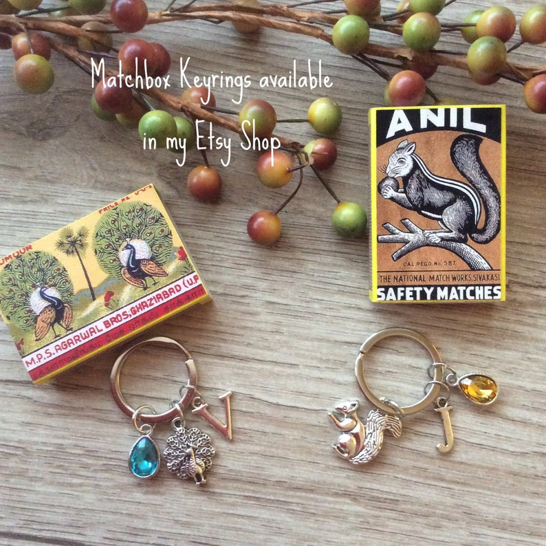 May include: Matchbox keyrings with charms, including a peacock, squirrel, and initial pendants. The image also shows vintage matchboxes with peacock and squirrel illustrations. Text on the image reads "Matchbox Keyrings available in my Etsy Shop."