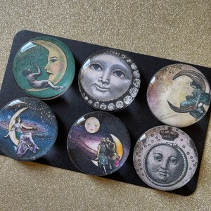 Peut inclure: Six ornements ronds en verre avec des images de lune et d'&eacute;toiles. Les ornements pr&eacute;sentent une vari&eacute;t&eacute; de motifs, notamment une lune croissante avec une femme assise dessus, une pleine lune avec un visage et un couple debout sur une lune croissante. Le texte "Love you to the moon and back" est sur l'un des ornements.