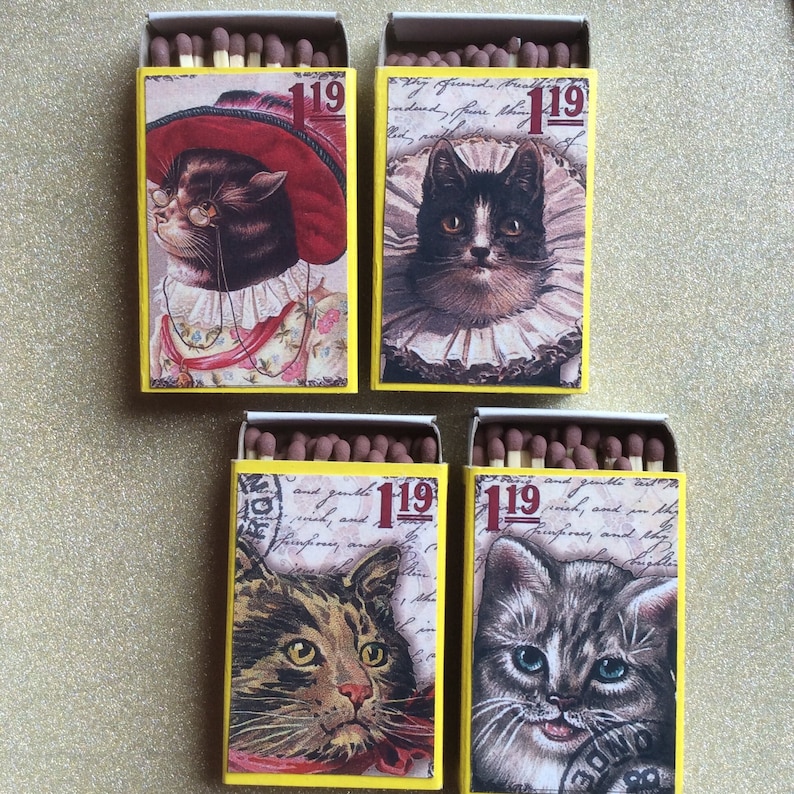 May include: Four vintage matchboxes with yellow and white backgrounds. Each box features a different illustration of a cat with a unique design. The boxes are labeled with the number "119".
